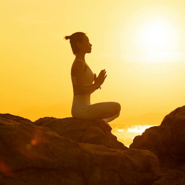 Silhouette of a person in a warrior yoga pose against a rising sun.